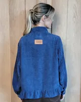 Sobrecamisa de pana color marrón oscuro, con cuello camisero, cierre frontal de botones y detalle de volado en el ruedo. Presenta mangas largas con puños y bolsillos frontales aplicados.
