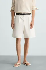 Bermuda de corte regular fit, color blanco hueso, confeccionada en tejido de algodón y lino. Presenta pliegues frontales, bolsillos delanteros y bolsillos traseros de plastrón.