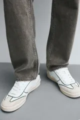 Zapatilla deportiva de estilo retro, color negro, con parte superior fabricada en combinación de piezas de cuero liso y gamuza perforada. Presenta una suela de goma en color marrón oscuro o ahumado en contraste.