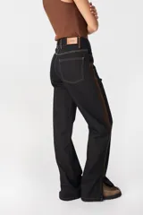 Jean de tiro alto y pierna recta, confeccionado en denim color azul oscuro. Presenta una franja lateral en tono marrón, costuras en contraste y tajos en el ruedo. Cuenta con diseño de cinco bolsillos y cierre frontal.