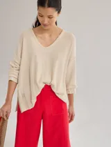 Buzo de tejido de punto liviano en color beige, con escote en V y diseño holgado. Presenta costuras visibles en los hombros y un detalle bordado en el lateral inferior.