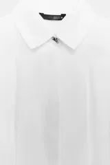 Camisa de popelín color celeste, con cuello solapa, manga larga y cintura entallada con pliegues. Presenta cierre frontal con botones ocultos por solapa.