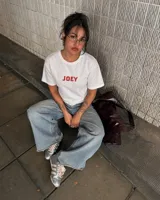 Remera de manga corta blanca con diseño gráfico en la espalda estilo estampilla que muestra una fotografía en blanco y negro de una persona con un gato, acompañada del logotipo rojo de Kaboa Industries.