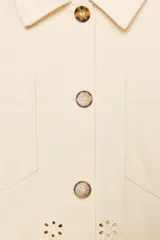 Cazadora color rosa pálido, de cuello solapa y manga larga. Tiene bordados perforados a tono en el ruedo y cierre frontal con botones color madera.