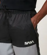 Bermuda deportiva de tejido plano de poliamida, color negro y gris claro, con bloques de color reflectivo en la parte inferior. Presenta cintura elástica con amarre y un pequeño logo de la NASA en la pierna derecha.
