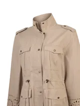 Chaqueta estilo militar beige, confeccionada en algodón orgánico. Cuenta con cuello alto, cierre frontal con cremallera y botones a presión, múltiples bolsillos con solapa en el pecho y la cintura, cordón ajustable en la cintura y detalles de diseño calado en los puños de las mangas largas.