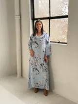 Vestido largo celeste con estampado floral en tonos blancos y grises, de corte holgado, mangas largas y cuello drapeado.