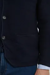 Cardigan tejido color azul marino, con cuello y solapa, cierre frontal de botones y bolsillos delanteros. Presenta un tejido de punto con textura.