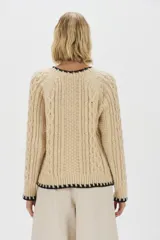 Sweater de punto de mohair color beige, con cuello redondo, mangas largas y detalles de terminación en color negro en el cuello, puños y ruedo.