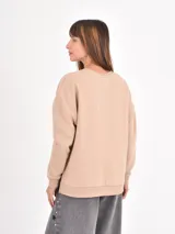 Buzo de cuello redondo, manga larga con puños elásticos y diseño holgado. Presenta un corte asimétrico con aberturas laterales en el ruedo.