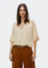 Blusa color crema/beige claro, de manga corta ancha tipo mariposa y escote pronunciado en V.