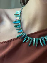 Collar corto con bastones de nácar teñidos en tonos turquesa y verde iridiscente, intercalados con pequeñas mostacillas transparentes. Se ajusta con cadena de acero quirúrgico y gancho.