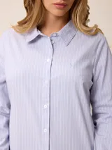 Camisa de corte clásico y calce entallado, color blanco, con cuello camisero, cierre frontal de botones y mangas largas con puños abotonados. Presenta un pequeño bordado distintivo en el pecho.