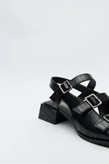 Sandalia negra de cuero sintético con textura símil reptil, taco medio cuadrado y múltiples tiras con hebillas metálicas ajustables.