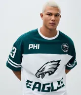Remera de corte oversized con diseño deportivo de los Philadelphia Eagles. Presenta cuello redondo, mangas cortas con detalles de rayas y estampa frontal del equipo. Confeccionada en algodón.