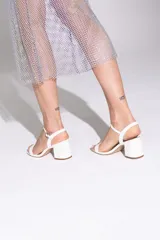 Sandalias blancas de tiras finas, con taco ancho y bajo. Presentan una tira fina en la parte delantera y una tira con hebilla ajustable en el tobillo.