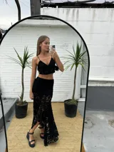 Pollera larga asimétrica color negro, confeccionada en encaje con detalles de terciopelo, de tiro alto y diseño con movimiento y vuelo en el bajo.