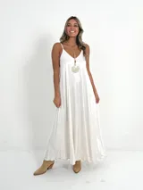 Vestido largo blanco de breteles finos y escote en V, confeccionado en tela nacarada.