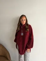 Buzo de corderito color marrón, con cuello alto y cierre frontal parcial. Presenta un diseño holgado con mangas largas y un parche decorativo en el frente.