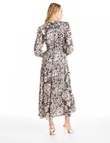 Vestido maxi de satén con estampado floral en tonos negro y beige. Presenta escote en V, hombros fruncidos, mangas largas con puños elásticos y cintura con detalle de punto smock. La falda tiene un diseño escalonado con vuelo.