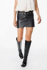 Mini falda tipo cruzada confeccionada en cuero, con detalle de cintura con tachas metálicas.