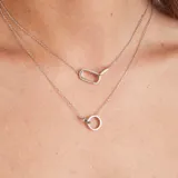 Conjunto de dos collares en plata 925. El collar superior presenta un dije rectangular con engarce de circones. El collar inferior presenta un dije circular liso. Además, la modelo lleva aros pequeños de plata 925.