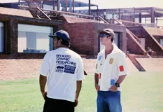 Camisa blanca de manga corta con parches de tela de colores (azul, rojo, amarillo) distribuidos irregularmente.