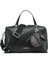 Cartera tipo satchel de Calvin Klein en color negro, confeccionada en material sintético con textura granulada. Presenta doble asa de mano, correa de hombro ajustable y extraíble, y cierre superior con cremallera. Incluye accesorios colgantes decorativos: un monedero circular y un pequeño estuche con solapa, ambos con el monograma de la marca.