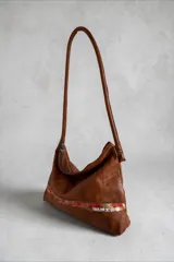 Cartera de cuero 100% natural color marrón, con diseño de hombro, cierre superior y detalles de arte pintado en la parte inferior.