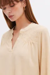 Blusa blanca de viscosa con detalles de broderie en los hombros, cuello en V y mangas largas holgadas.