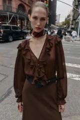 Vestido midi de color marrón con diseño combinado, escote en pico con volantes, mangas largas con puños elásticos y falda evasé. Incluye un cinturón negro con hebilla dorada en la cintura y cierre lateral con cremallera oculta.