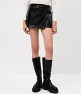 Short pollera de tiro alto confeccionado en poliuretano con acabado que imita el cuero. Presenta un diseño cruzado tipo falda con cinturón integrado de hebilla metálica y cierre oculto.