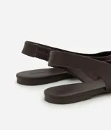 Zapatilla tipo slingback de cuero color marrón oscuro, con diseño de punta fina y talón descubierto con tira de ajuste.