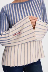 Sweater de punto con diseño de rayas verticales en relieve, combinando colores azul y crudo. Presenta mangas largas acampanadas con un detalle bordado en color rojo en la parte inferior.