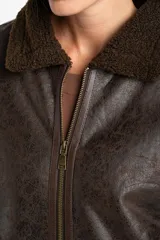 Campera tipo gamulán de corte oversize, color marrón oscuro con efecto cuero envejecido. Presenta cuello solapa, puños y ruedo con forro de corderito sintético en tono marrón oscuro. Cuenta con cierre frontal completo y detalles de costuras reforzadas.