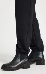 Pantalon tipo jogger de tiro alto, color negro, confeccionado en tejido de punto. Presenta una cinturilla elástica ancha con cordón ajustable y detalle de superposición de encaje en la parte delantera. Cuenta con bolsillos laterales ribeteados, perneras ligeramente holgadas y puños ajustados con elástico.