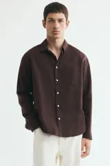 Camisa de manga larga color marrón, con cuello inglés, cierre frontal de botones, bolsillo en el pecho y bajo redondeado. Confeccionada en mezcla de algodón y lino.