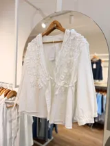 Blusa cruzada confeccionada en lino color blanco, con escote en V y delicados volados en el delantero y la espalda. Cuenta con mangas largas y sistema de ajuste mediante lazo lateral.