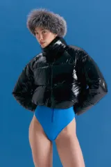 Campera puffer corta de color negro con acabado brillante, cuello alto y cierre frontal. Confeccionada en poliamida, presenta un diseño acolchado con bolsillos delanteros con cierre invisible.