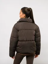 Campera puffer corta Umbro de color negro, con cuello alto, cierre frontal y bolsillos laterales. Presenta un diseño acolchado y logo de la marca bordado en el pecho.