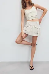 Falda pantalón satinada de tiro medio y color negro, con bolsillos cargo de plastrón con solapa, pliegues decorativos en el delantero y cierre lateral con cremallera oculta.