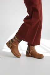 Bota estilo biker de caña media, confeccionada en cuero negro con detalles en gamuza marrón. Presenta correas ajustables con hebillas metálicas, tachas decorativas y suela track dentada.