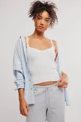 Musculosa blanca de tejido acanalado con detalles de encaje festoneado en el escote y los tirantes, corte ajustado y ruedo con terminación ondulada.