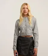 Cardigan cropped de punto color gris, con cuello redondo, manga larga, cierre frontal con botones y dos bolsillos delanteros. Presenta terminaciones acanaladas en puños y bajo.