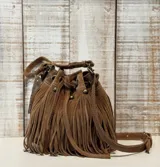 Cartera tipo bucket bag de gamuza color marrón, con diseño de flecos largos en todo el cuerpo, detalles de tachas metálicas y cierre mediante cordón ajustable.