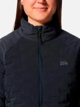 Campera técnica de plumón para mujer, color gris oscuro, con diseño de compartimentos elásticos integrados. Cuenta con cierre frontal completo, cuello alto, bolsillos laterales con cierre y puños con ribete elástico. Es una prenda compresible diseñada para actividades de montaña y senderismo.