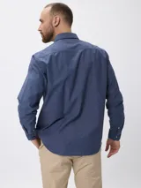 Camisa de manga larga en algodón tramado, con cuello clásico abotonado y cierre frontal con botones. Presenta un diseño liso con textura visible y un pequeño bordado en la pechera.