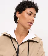 Campera cortaviento Marfinno de color beige, diseño corto con capucha, cierre frontal de cremallera con tiradores negros, bolsillos laterales y elástico fruncido en el ruedo y los puños.