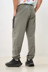 Pantalón deportivo gris con paneles laterales negros, cintura elástica y puños ajustados.