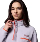 Buzo de polar tipo sherpa color lila, con cuello alto y cierre frontal parcial con botones a presión. Presenta detalles en color naranja en los bordes, puños y bolsillo frontal con cierre en el pecho. Incluye logo de la marca bordado.